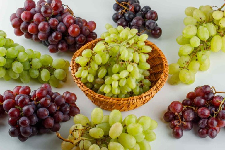 Mixed grapes arranged around a wicker basket on white background.