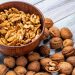Walnut halves in wooden bowl surrounded by whole walnuts.