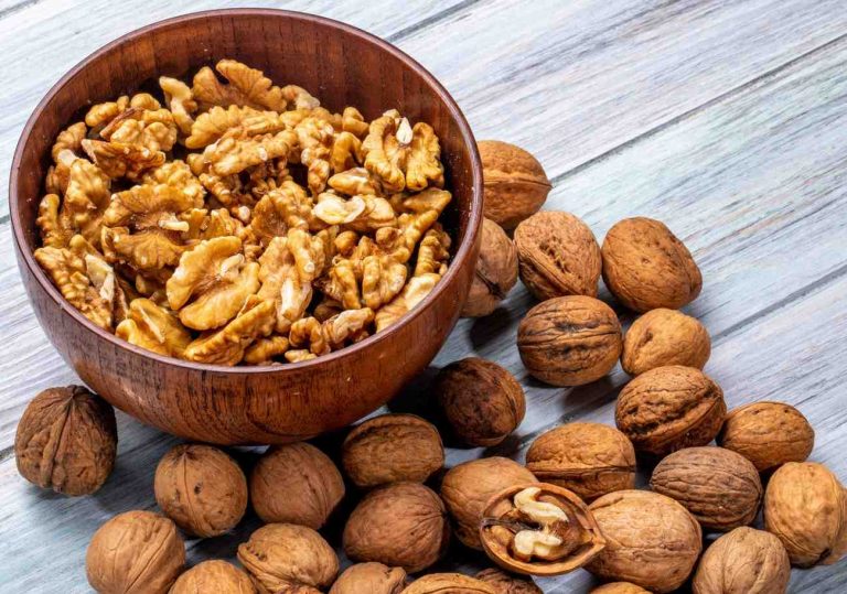 Walnut halves in wooden bowl surrounded by whole walnuts.