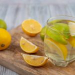 Glass of lemon water with sliced lemons and limes on a wooden board.