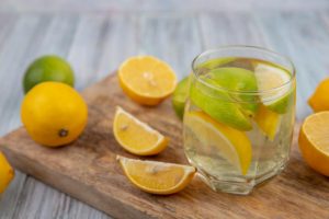 Glass of lemon water with sliced lemons and limes on a wooden board.