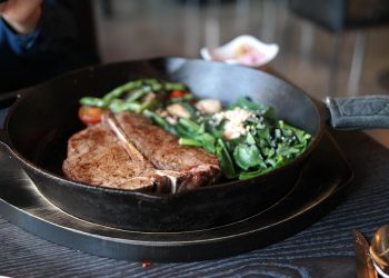 Grilled T-bone steak with vegetables in cast iron skillet.