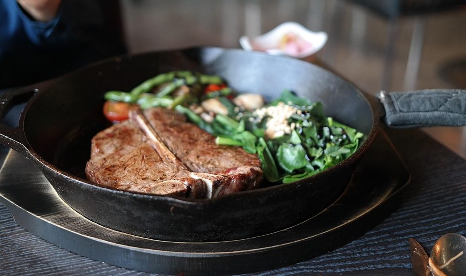 Grilled T-bone steak with vegetables in cast iron skillet.