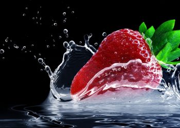 Strawberry splashing into water with droplets frozen in motion.