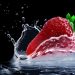 Strawberry splashing into water with droplets frozen in motion.