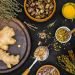 Ginger and herbs on a dark surface with various spices displayed.