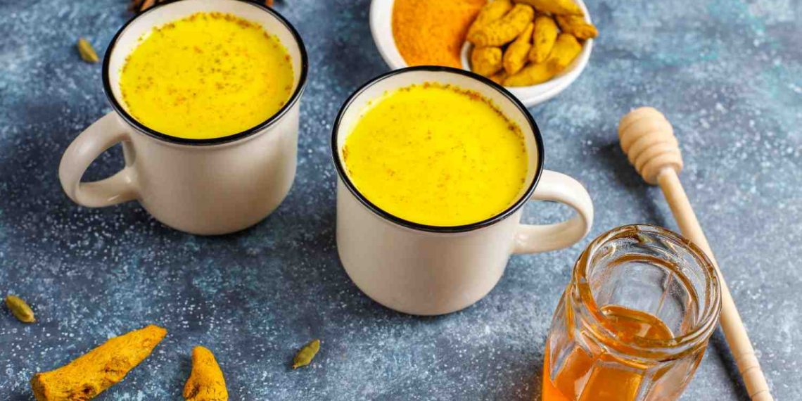 Two mugs of turmeric latte with spices and honey on a blue surface.