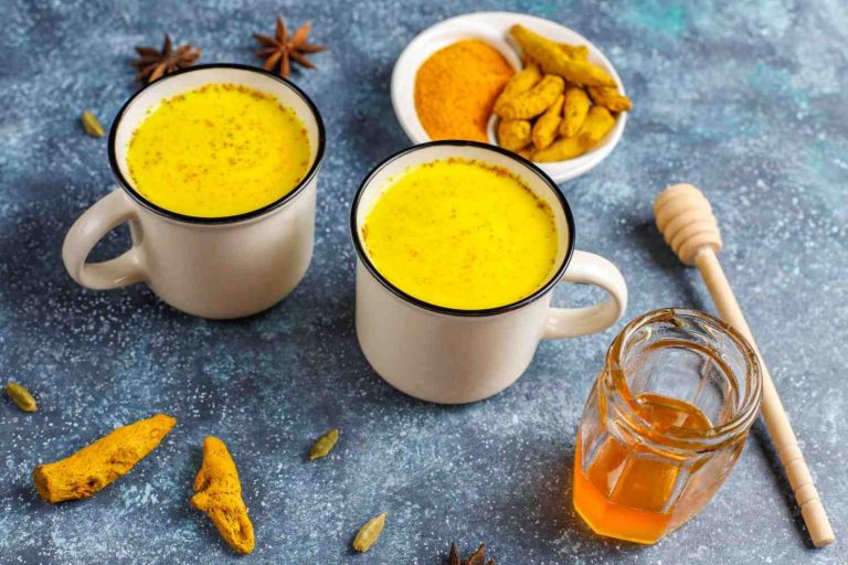 Two mugs of turmeric latte with spices and honey on a blue surface.