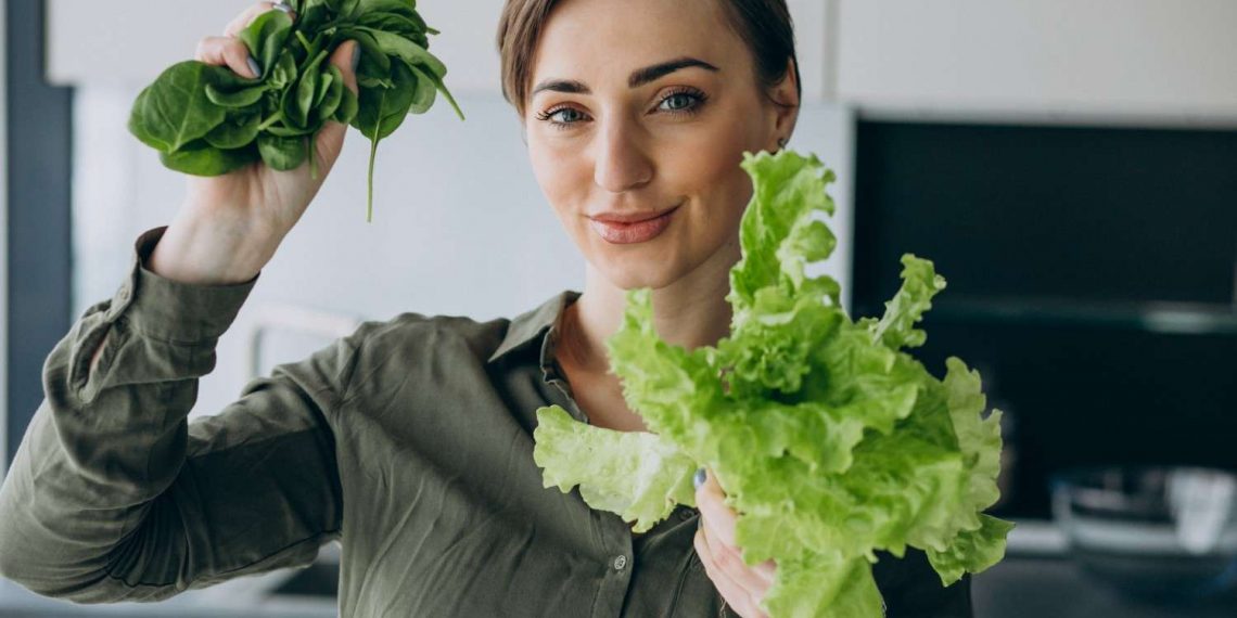 Woman holding fresh spinach, basil and lettuce in kitchen.