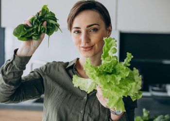 Woman holding fresh spinach, basil and lettuce in kitchen.