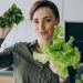 Woman holding fresh spinach, basil and lettuce in kitchen.