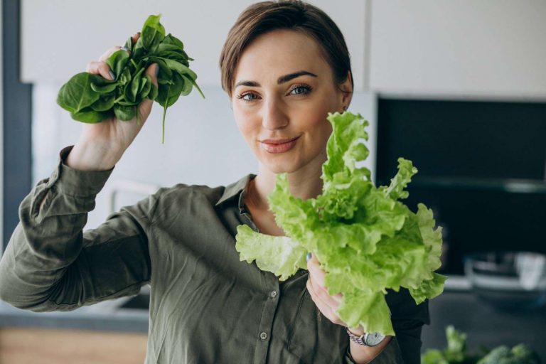 Woman holding fresh spinach, basil and lettuce in kitchen.