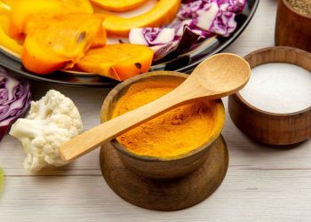 Turmeric in a wooden bowl with fresh vegetables nearby.