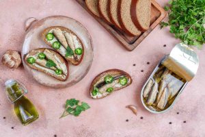 Sardine toasts with jalapeños and parsley on a plate with sliced bread.