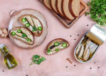 Sardine toasts with jalapeños and parsley on a plate with sliced bread.