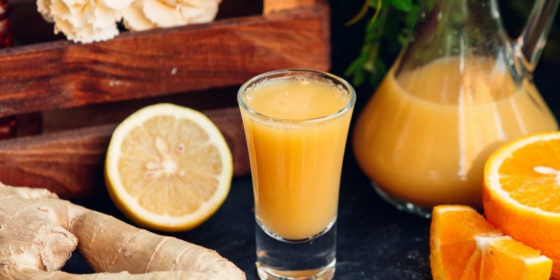 Ginger citrus juice in a glass with fresh lemon and orange slices.