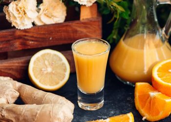 Ginger citrus juice in a glass with fresh lemon and orange slices.
