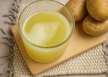 Potato juice in a glass on a wooden board near whole potatoes.