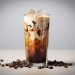 Iced coffee with cream swirl in a tall glass surrounded by coffee beans.
