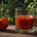 Tomato next to glass of fresh tomato juice on a wooden surface.