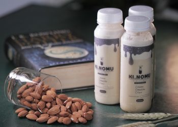 Almonds spilled next to bottles of Ki Nomu almond milk and a book.