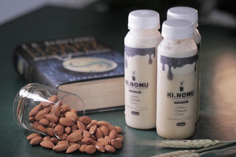 Almonds spilled next to bottles of Ki Nomu almond milk and a book.