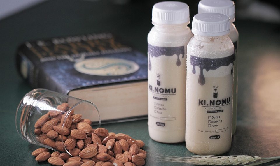 Almonds spilled next to bottles of Ki Nomu almond milk and a book.