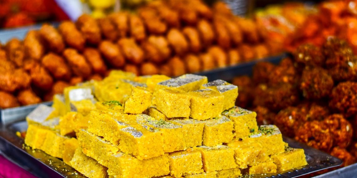 Indian sweets on a tray at a market stall with vibrant colors.