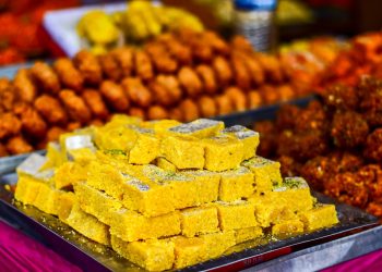 Indian sweets on a tray at a market stall with vibrant colors.