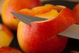 Knife peeling red apple skin smoothly.