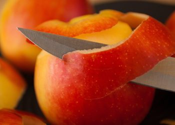 Knife peeling red apple skin smoothly.