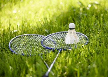Badminton rackets and shuttlecock resting on grass.