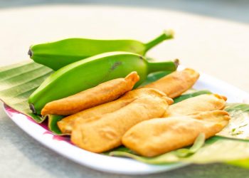 Fried bananas served on banana leaves with fresh bananas.
