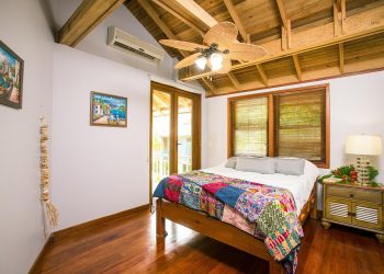 Cozy bedroom with wooden ceiling fan and colorful quilt.