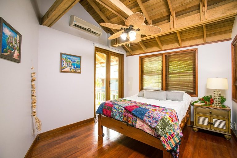 Cozy bedroom with wooden ceiling fan and colorful quilt.