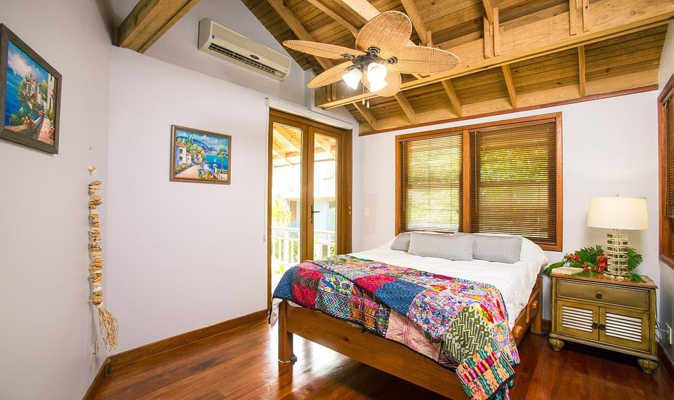 Cozy bedroom with wooden ceiling fan and colorful quilt.