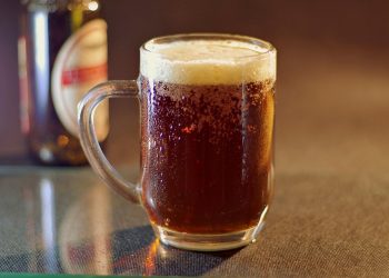 Frosty mug of dark beer with foam on a table.