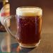 Frosty mug of dark beer with foam on a table.