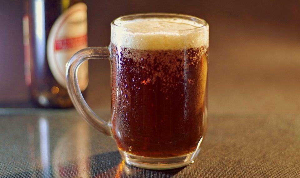 Frosty mug of dark beer with foam on a table.