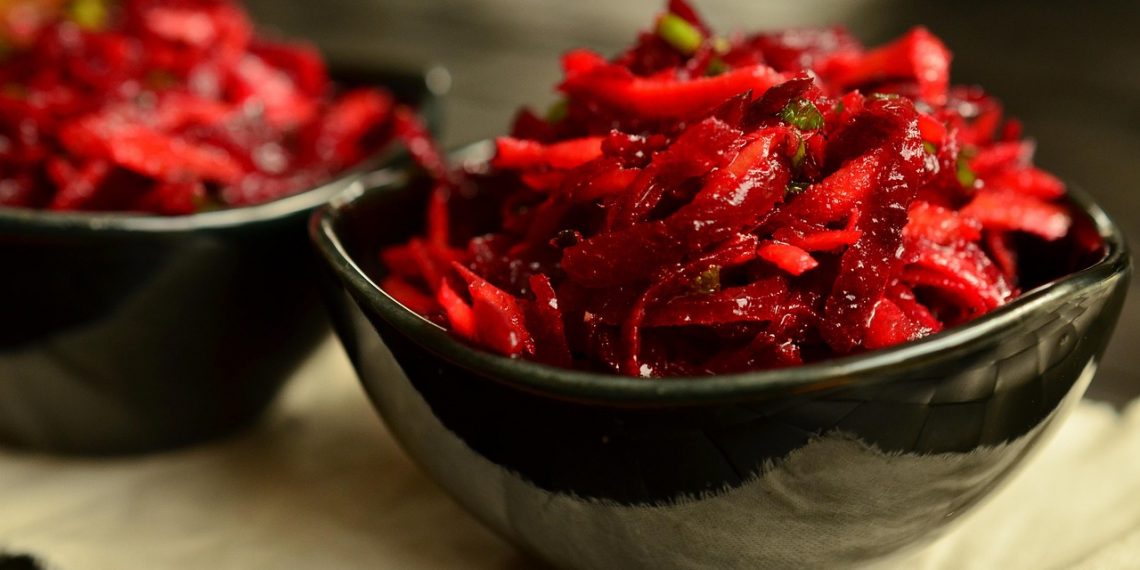 Shredded beet salad in a black bowl, garnished with fresh herbs.