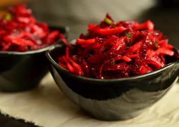 Shredded beet salad in a black bowl, garnished with fresh herbs.
