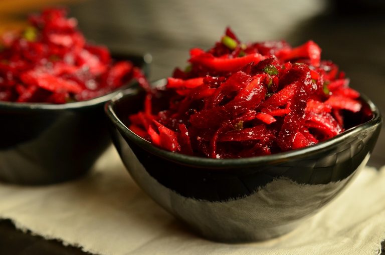 Shredded beet salad in a black bowl, garnished with fresh herbs.