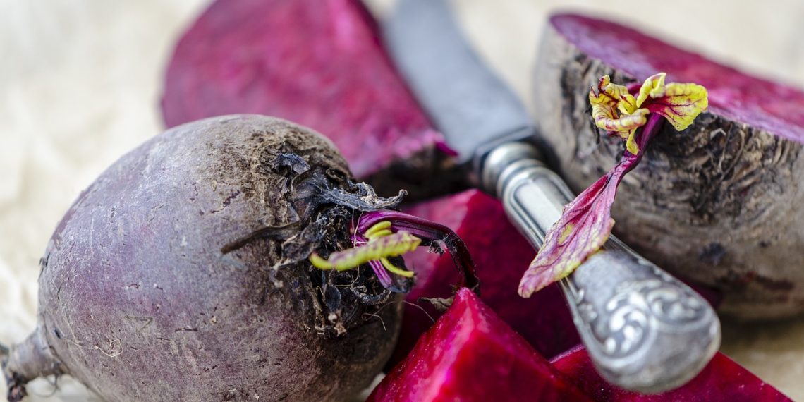Whole and sliced beets with knife on a table.