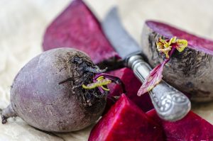 Whole and sliced beets with knife on a table.