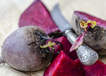 Whole and sliced beets with knife on a table.