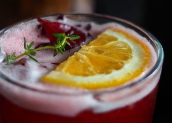 Refreshing hibiscus cocktail garnished with orange slice.