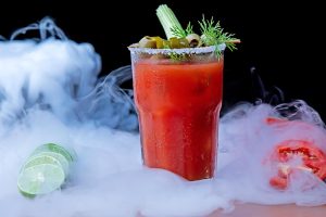 Bloody Mary cocktail with celery and olives in a smoky setting.
