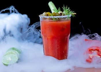 Bloody Mary cocktail with celery and olives in a smoky setting.