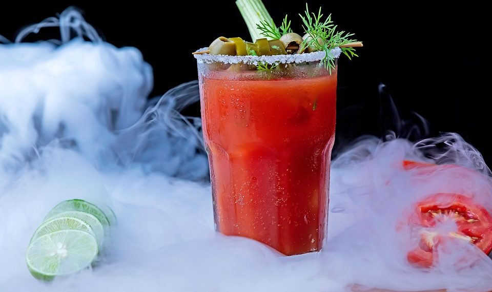 Bloody Mary cocktail with celery and olives in a smoky setting.
