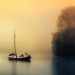 Sailboat on misty lake at sunrise near trees.
